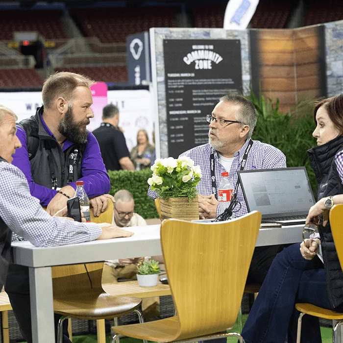 Three gentleman talking on the show floor around a red table